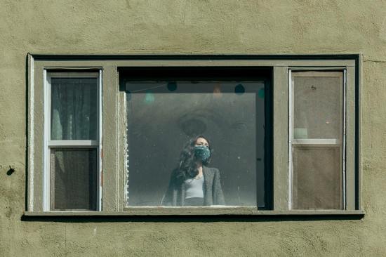 Woman covering her mouth with a bandana staring out the window during the coronavirus lockdown